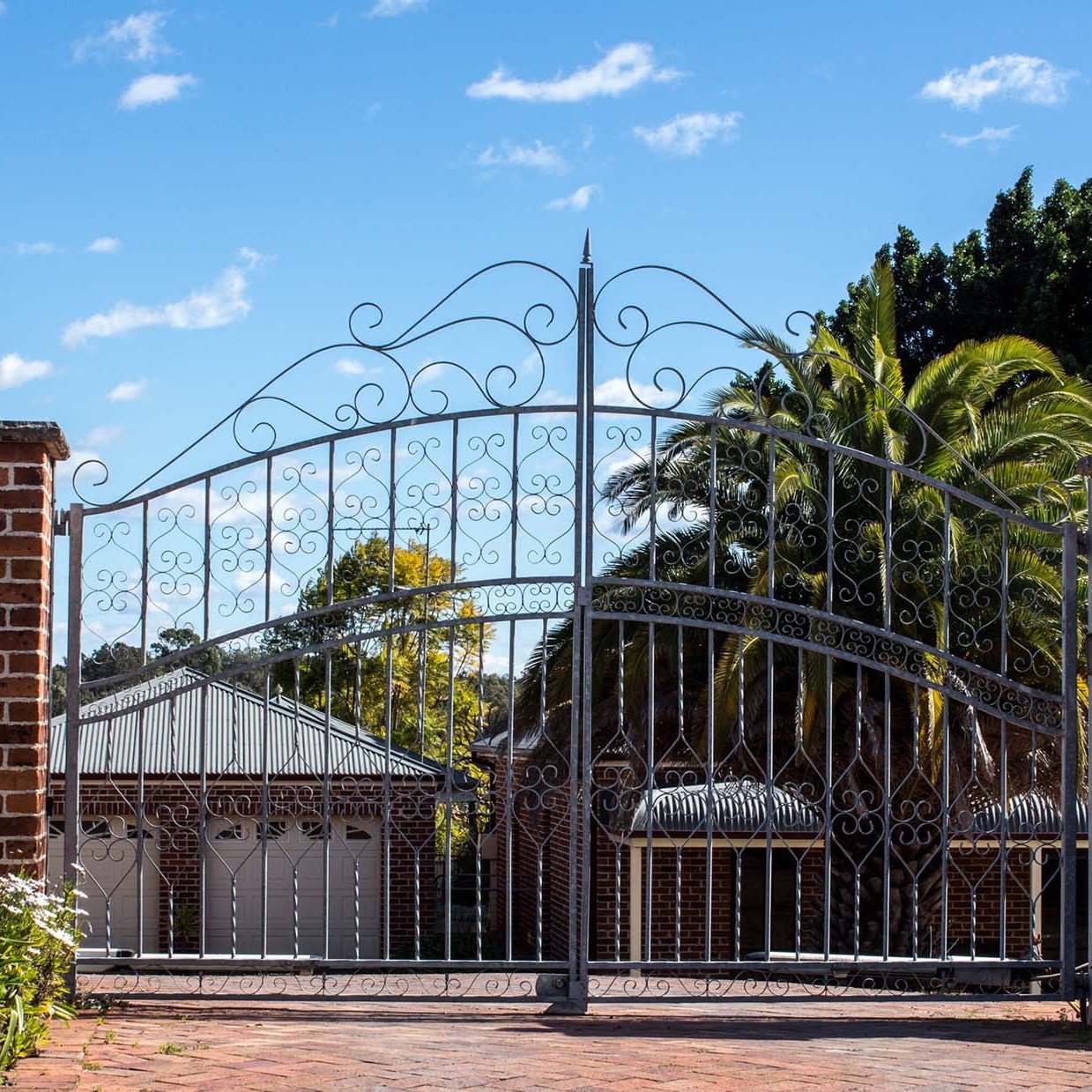 Metal driveway security entrance gates set in brick fence with residential garden